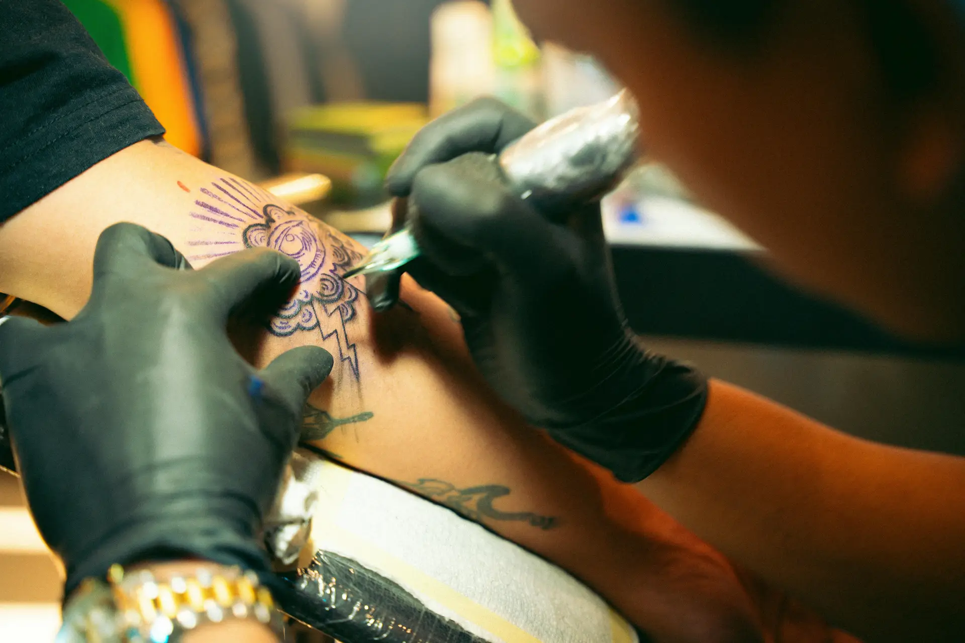 Tri-State Beauty Hub 39 Artist meticulously applying a tattoo on a person's arm in a studio.